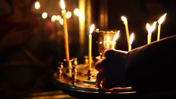 A man corrects burning candles in front of an Orthodox icon — Stock Video