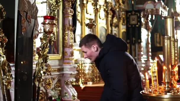 Den unge mannen pilbågar och kyssar korset i den ortodoxa kyrkan — Stockvideo