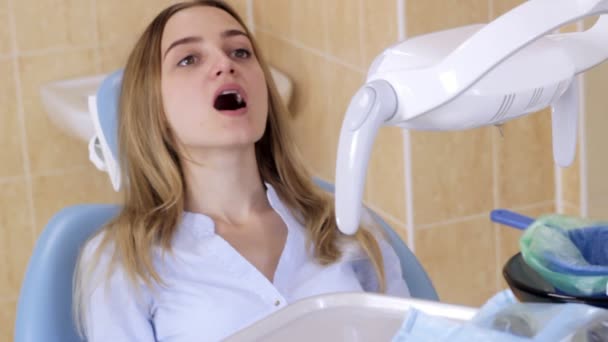 The patient girl at the dentist with his mouth open, spits in the trash — Stock Video