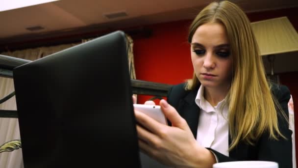 Chica de negocios en la cafetería con ordenador portátil y teléfono inteligente en busca de información en Internet en su teléfono — Vídeos de Stock