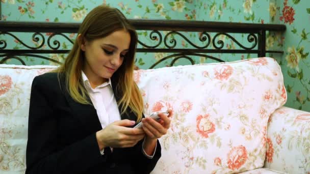 Joven mujer de negocios en traje utiliza teléfono inteligente en el sofá — Vídeos de Stock