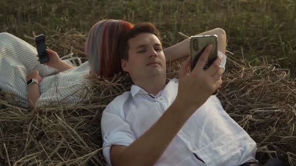 Мужчина и женщина лежат на сене и смотрят в смартфоны — стоковое видео