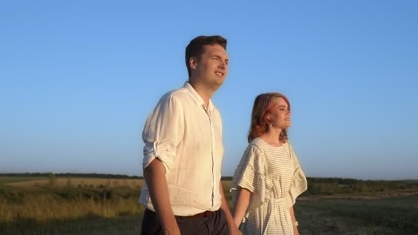 Milující pár kráčí přes pole, drží se za ruce a usmívá se — Stock video