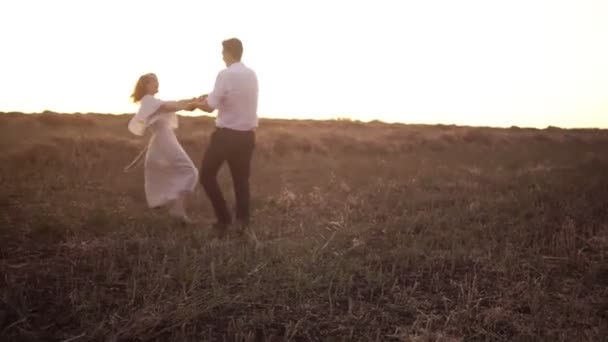 Hombre y mujer enamorados giran tomados de la mano en el campo — Vídeo de stock