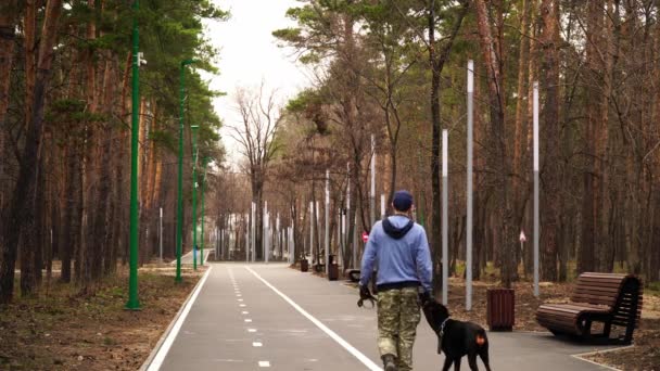 Egy maszkos férfi gyorsan sétál egy nagy doberman kutyával a sivatagi parkban. — Stock videók