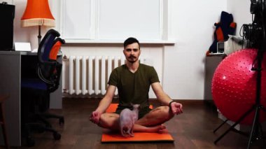 Erkek, ev ortamında dikkatlice meditasyon yapar kedi ona müdahale eder.