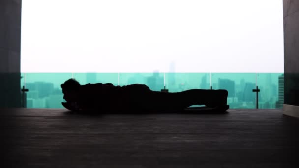 Silhueta de um homem fazendo flexões do chão no telhado de um edifício contra o fundo da metrópole — Vídeo de Stock