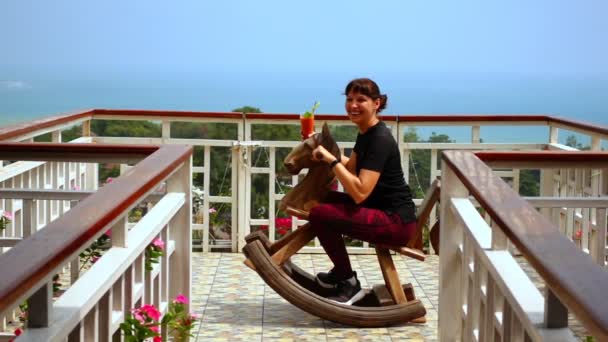 Młoda kobieta trzyma koktajl jadąc na koniu na balkonie — Wideo stockowe
