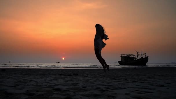 Szczęśliwa dziewczyna w sukience skacze po plaży o zachodzie słońca — Wideo stockowe