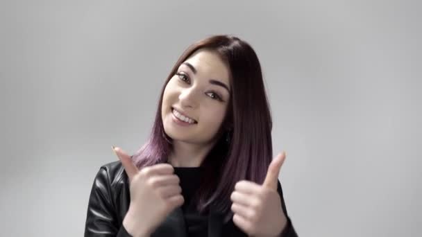 Портрет молодой женщины с фиолетовыми волосами, улыбающейся и показывающей большие пальцы в студии — стоковое видео