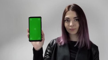 Elinde yeşil ekran olan telefonu tutan genç bir kadın onu izliyor ve işaret ediyor.