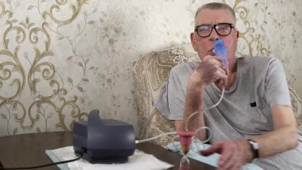 Elderly man breathes steam from a medical inhaler at home — Stock Video