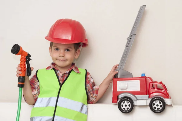 Niño en un casco rojo y con un camión de bomberos —  Fotos de Stock