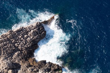 Mavi deniz, beyaz köpük ve gri kaya