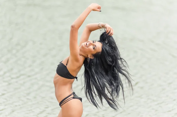 Hermosa chica morena posando en la playa en un traje de baño negro — Foto de Stock