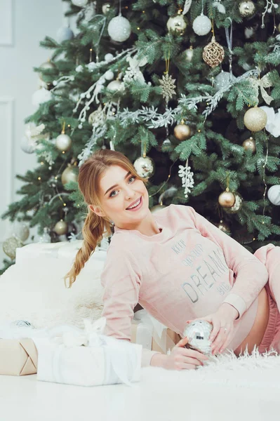 Happy young woman on Christmas holiday near beautiful Christmas tree with gifts