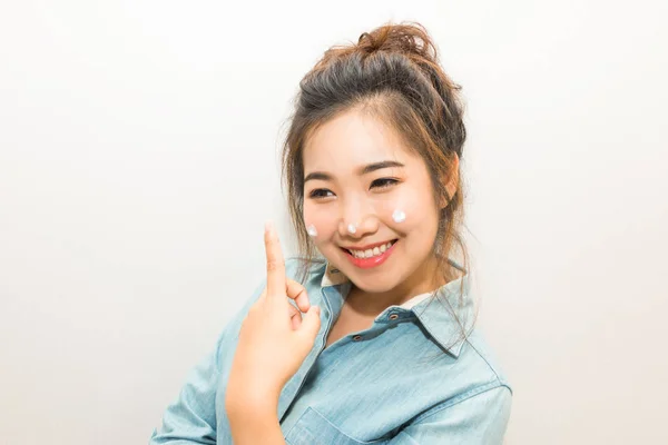 Joven mujer asiática sonriendo y aplicando crema hidratante en su —  Fotos de Stock