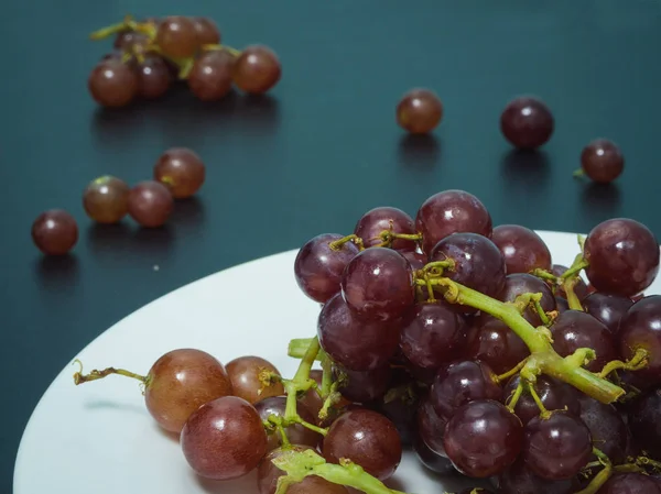 Fioletowy winogron na biały talerz na stole czarny — Zdjęcie stockowe
