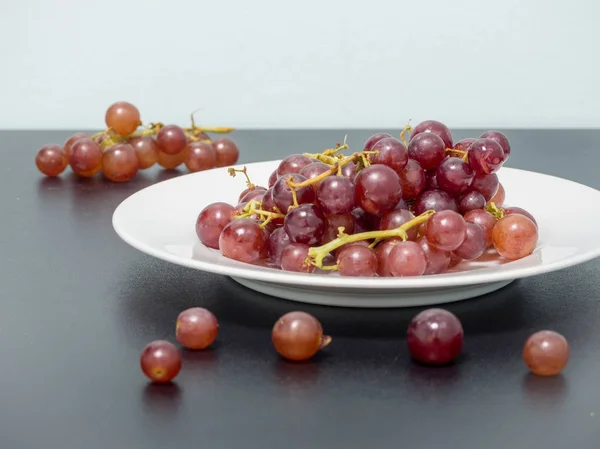 Violette Trauben auf weißem Teller auf schwarzem Tisch — Stockfoto