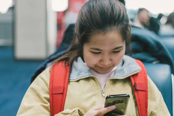 Female backpacker using smartphone and smilling between waiting