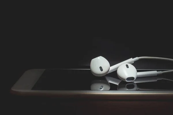 Earphones and smart phone on wooden table., Black and white tone