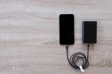 Tahta arka planda elektrik bankasıyla çalışan akıllı telefon..