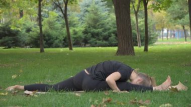 Kız yoga parkta yeşil çimenlerin üzerinde çalışmaktadır