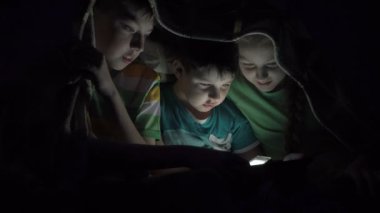 Yorganın altında tablet oynayan çocuklar