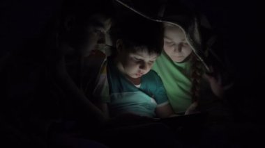 Yorganın altında tablet oynayan çocuklar