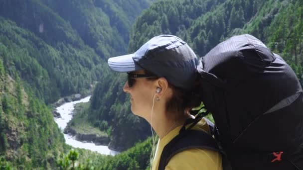 Menina ouvindo música com fones de ouvido em um fundo de montanhas — Vídeo de Stock