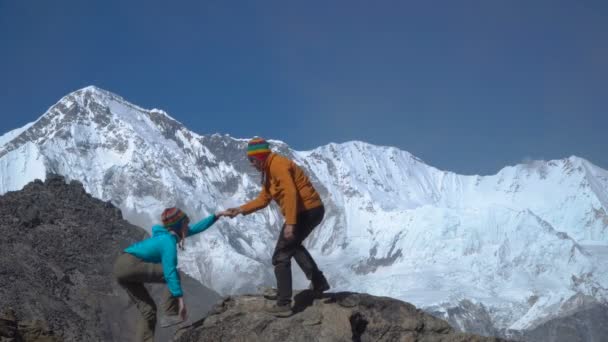 Un hombre ayuda a una chica a escalar una roca — Vídeos de Stock