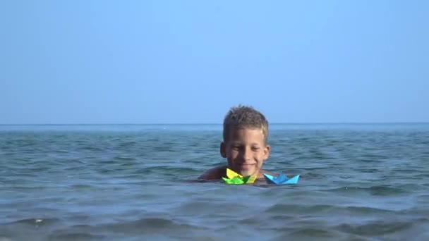 Маленькие дети запускают бумажную лодку в море — стоковое видео