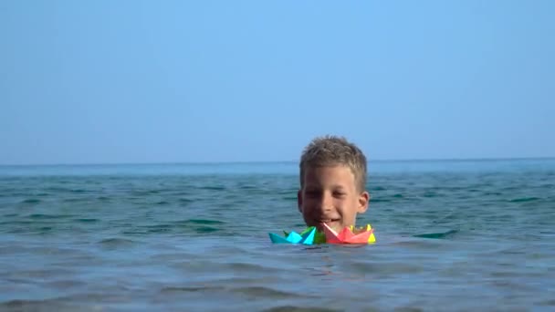 Маленькие дети запускают бумажную лодку в море — стоковое видео