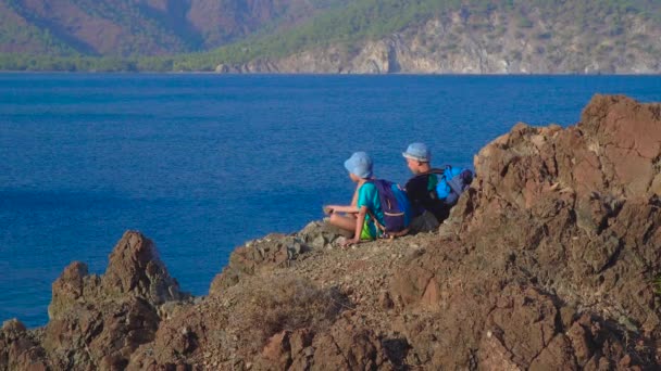 Los chicos están sentados en una roca a orillas del mar Mediterráneo. — Vídeo de stock