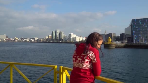 Una chica con el pelo largo mira a Reykjavik y el mar — Vídeo de stock