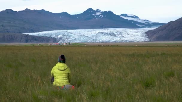 Bir kadın çimenlerde oturur ve İzlanda 'nın güzel doğasının tadını çıkarır.. — Stok video