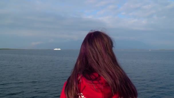 Portret van een jong mooi meisje op een achtergrond van blauwe zee en bergen. — Stockvideo