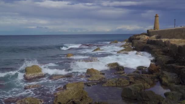 Las olas del mar chocan contra los rompeolas con un faro — Vídeo de stock