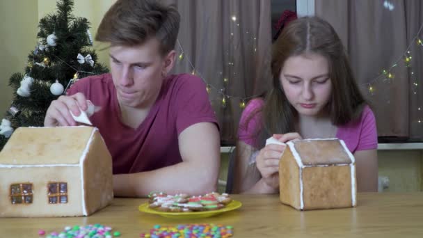 Egy fiú és egy lány díszítik a karácsonyi mézeskalács házat — Stock videók