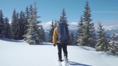 Sırt çantalı bir adam kış ormanında yürüyor.