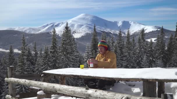 En man sitter och dricker te mot bakgrund av vinterlandskapet — Stockvideo
