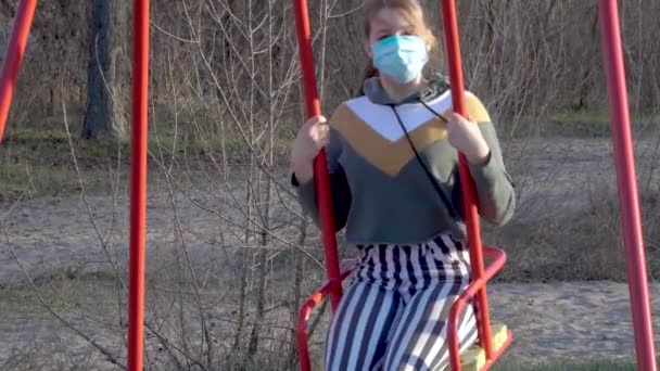 Девушка в медицинской маске на качелях — стоковое видео