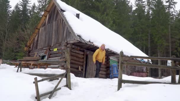 O viajante sai de uma casa de madeira na floresta de inverno — Vídeo de Stock