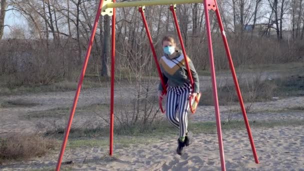 Meisje met een medisch masker op een schommel — Stockvideo