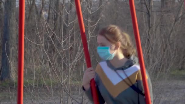 Meisje met een medisch masker op een schommel — Stockvideo