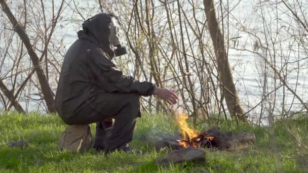 Muž v plynové masce smaží klobásu nad ohněm — Stock video