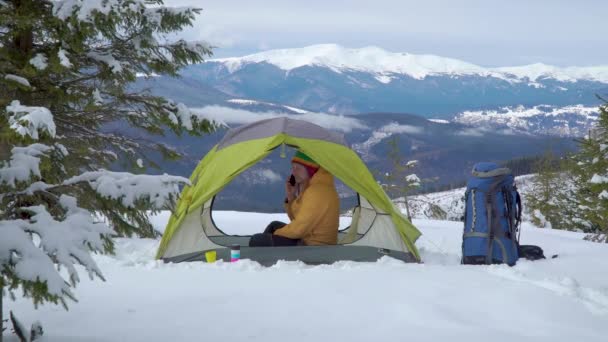 Un homme parle au téléphone dans une tente dans les montagnes en hiver — Video