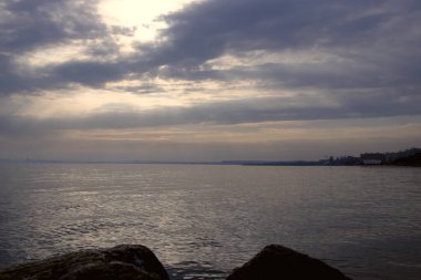 Gün batımı, alçak deniz manzarası, kara bulutlar.