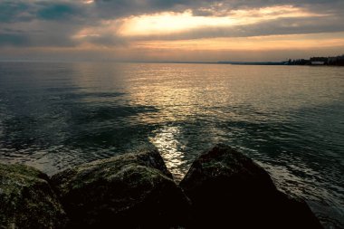 Gün batımı, alçak deniz manzarası, kara bulutlar.