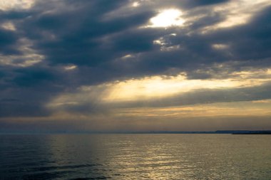 Gün batımı, alçak deniz manzarası, kara bulutlar.